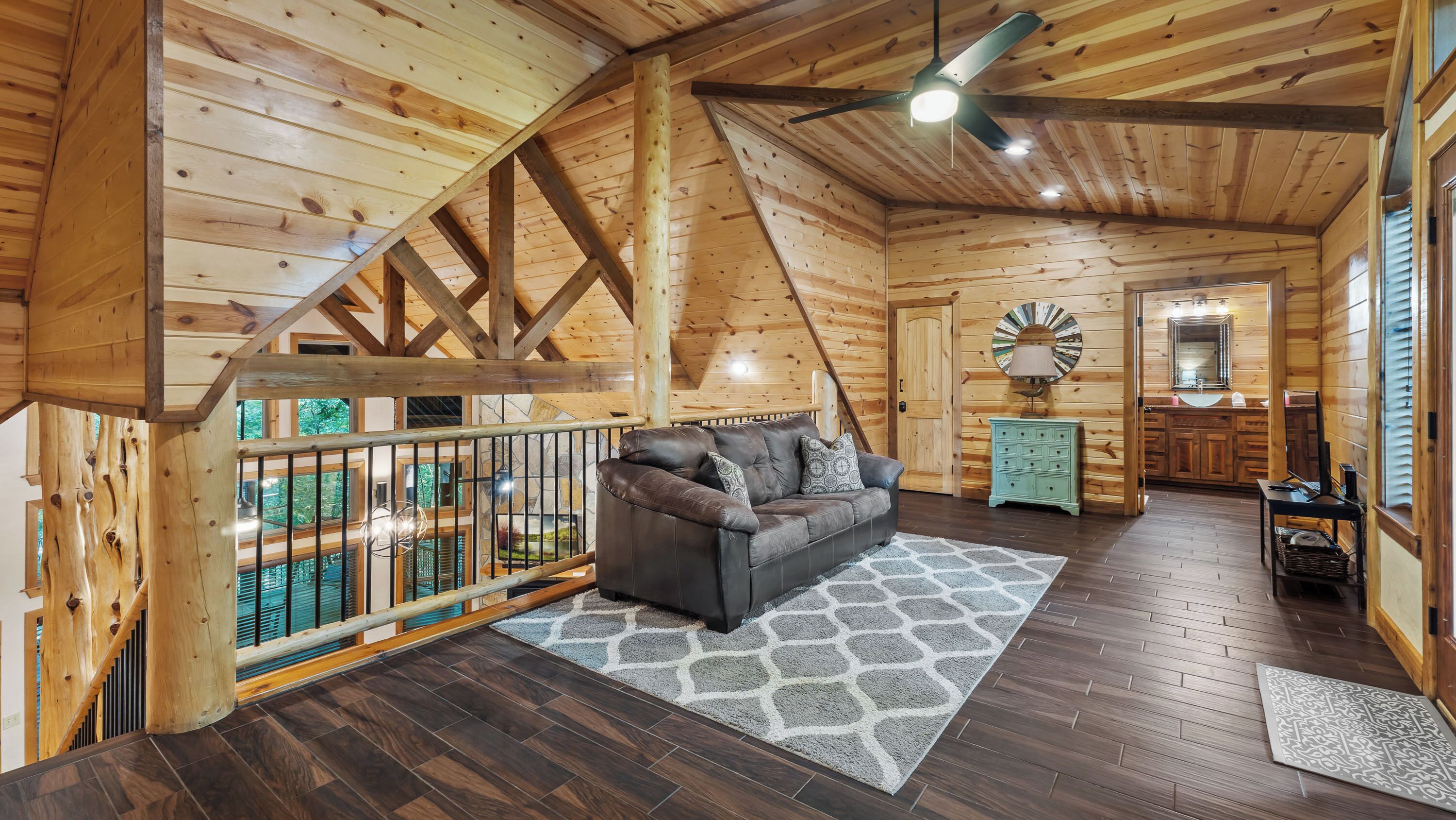 Een houten cabin interieur met een slaapkamer op een entresol, een woonkamer met een leren bank en een badkamer met een wastafel.