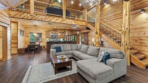 Ein geräumiges Blockhaus-Interieur mit einem großen grauen Ecksofa, einem Holzesstisch und einer Küchenzeile.