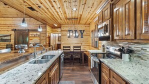 Ein Holzblockhaus-Interieur mit einer Küche, die sich durch Granit-Arbeitsplatten, Edelstahlgeräte und eine zentrale Kochinsel mit Sitzgelegenheit auszeichnet.
