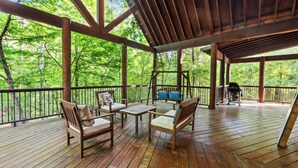 Eine Holzterrasse mit Gartenmöbeln, einem Grill und Blick auf einen Wald.