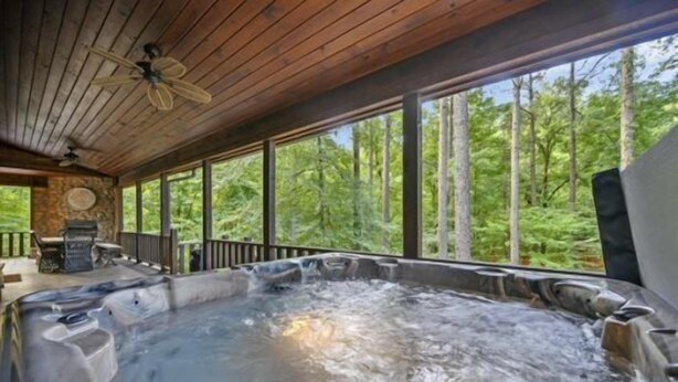 Un bain à remous doté d’un plafond en bois et de grandes fenêtres donnant sur une forêt.