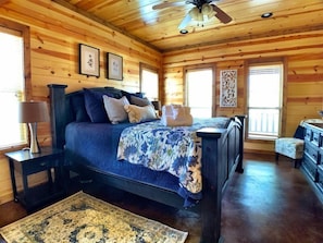 A wooden cabin bedroom with a bed, nightstands, a dresser, and a ceiling fan.