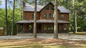 Une cabane en rondins à deux étages, avec des fondations en pierre, de grandes fenêtres et une véranda dotée d’une balustrade.