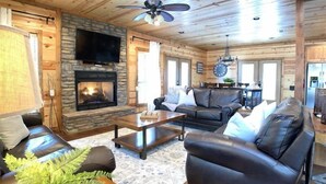 Un intérieur de chalet chaleureux avec une cheminée en pierre, des canapés en cuir et un téléviseur.