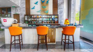 Zona de bar con tres sillas naranjas, un separador de madera y varios botellas y vasos en estantes.