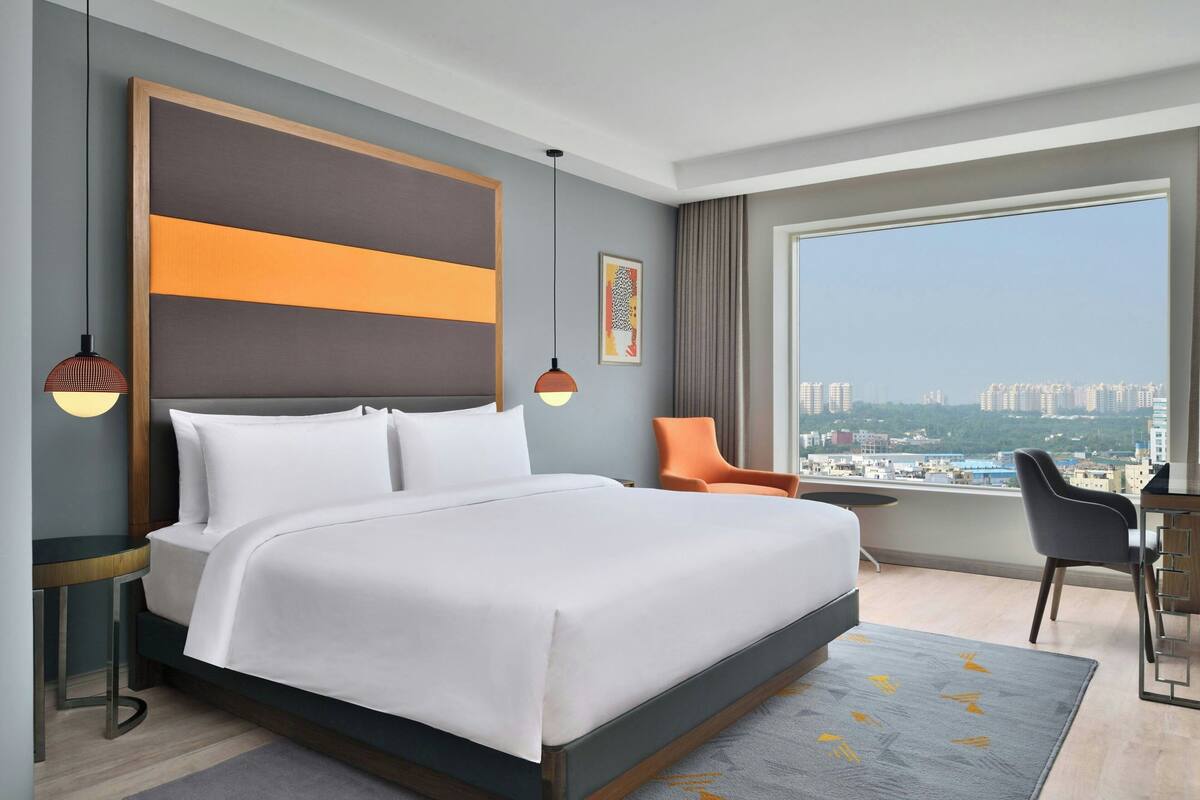 Ein modernes Hotelzimmer mit einem großen Bett, einem Schreibtisch und Blick auf die Stadt.