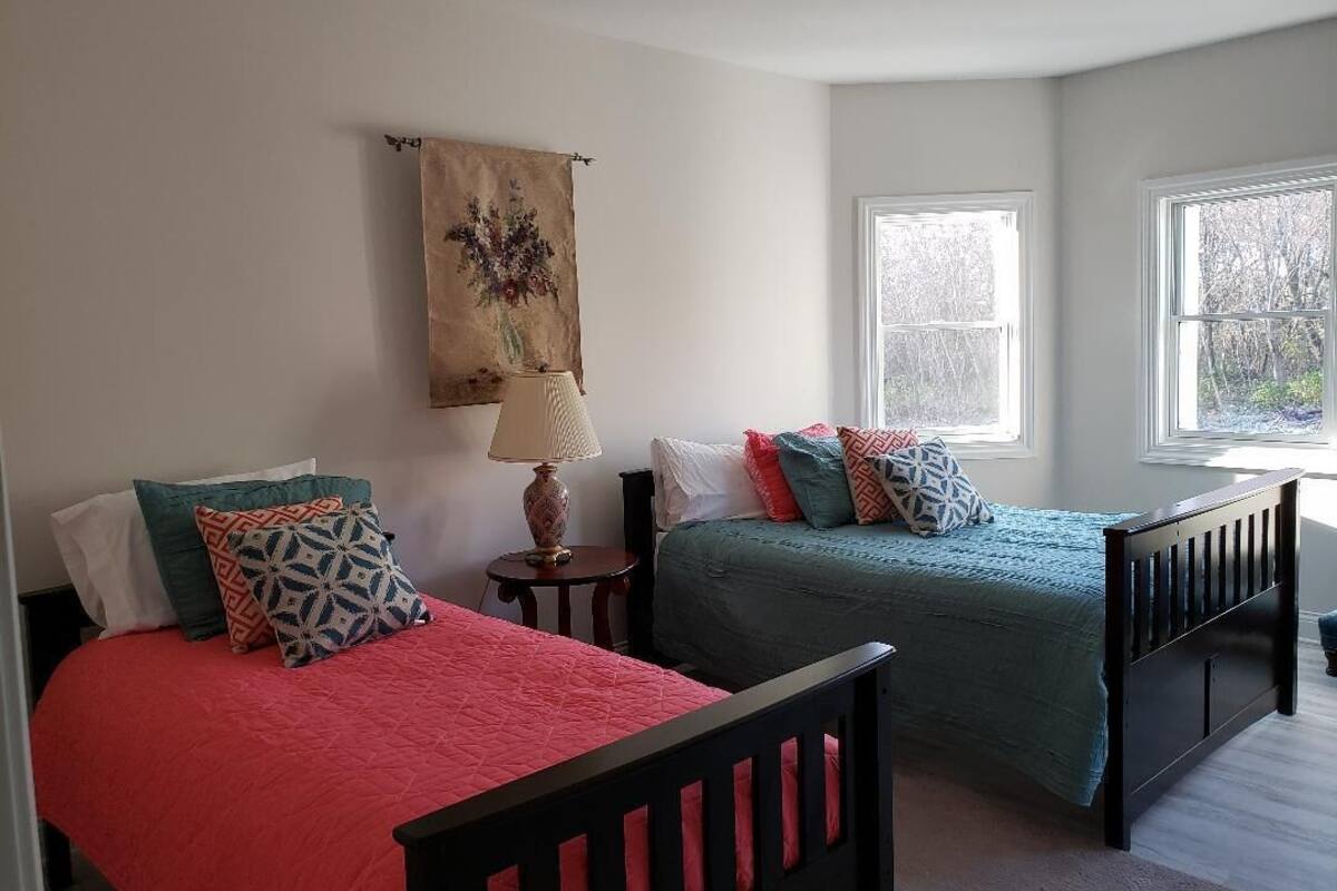 A bedroom with two beds, a nightstand, a lamp, and a tapestry on the wall.