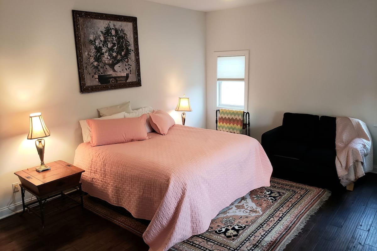 A bedroom with a bed, two bedside tables, a ceiling fan, a window, and a rug.