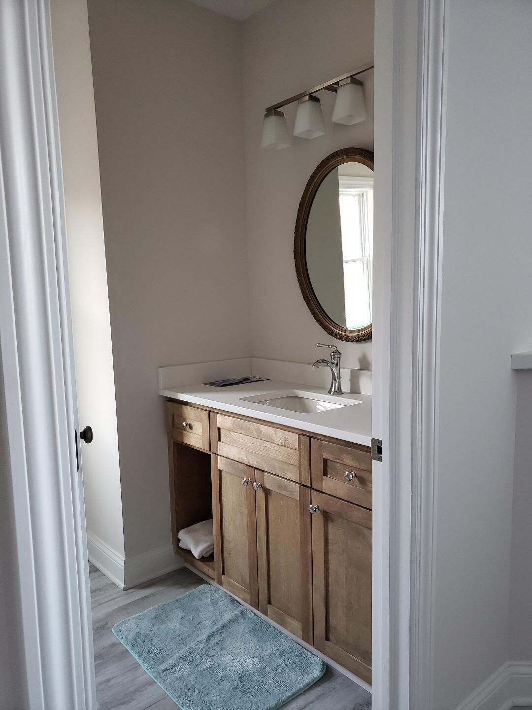 A bathroom with a white sink, wooden cabinets, a mirror, and a blue bath mat.
