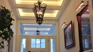 Ein Flur mit einer weißen Tür, einer Chandelüster und einem gerahmten Bild an der Wand.