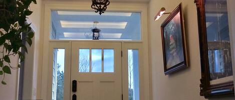 A hallway with a white door, a chandelier, and a framed picture on the wall.
