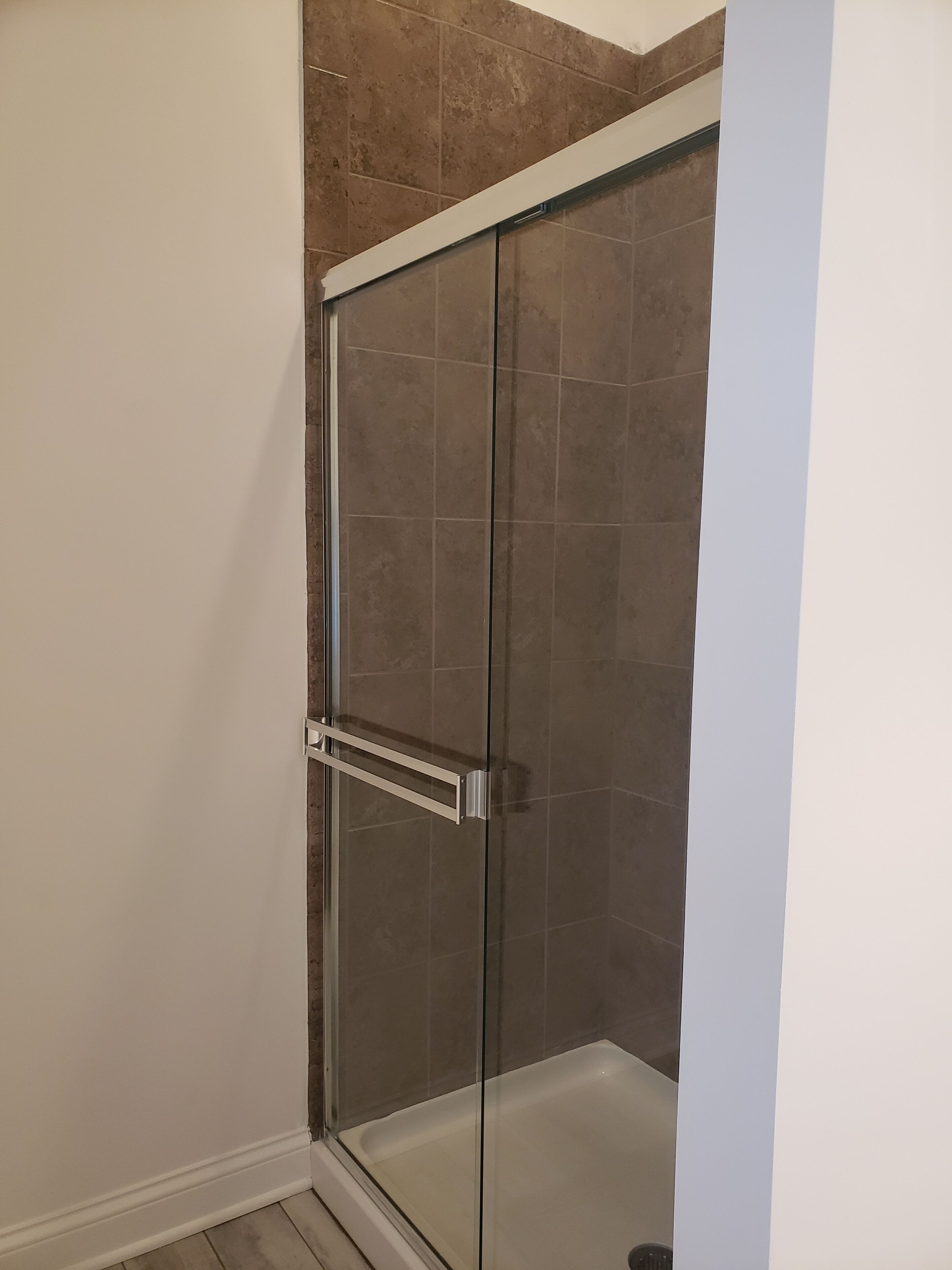 A glass-enclosed shower with a white door and a metal handle.