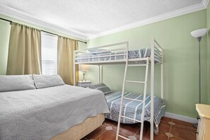 A bunk bed with a lower bunk, a bedside table with a lamp, and a window with curtains.
