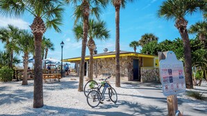 Um edifício à beira-mar com fachada de pedra, uma bicicleta estacionada em frente e uma placa indicando acesso à praia.