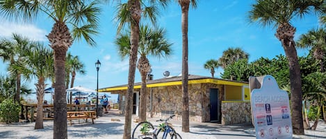 En byggnad vid stranden med en fasad av sten, en cykel parkerad framför och en skylt som visar var man kan komma åt stranden.