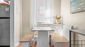 Cozinha compacta com geladeira, janela com persianas, um banco e uma mesa pequena.