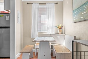Una cucina compatta con frigorifero, una finestra con persiane, una panca e un tavolino.