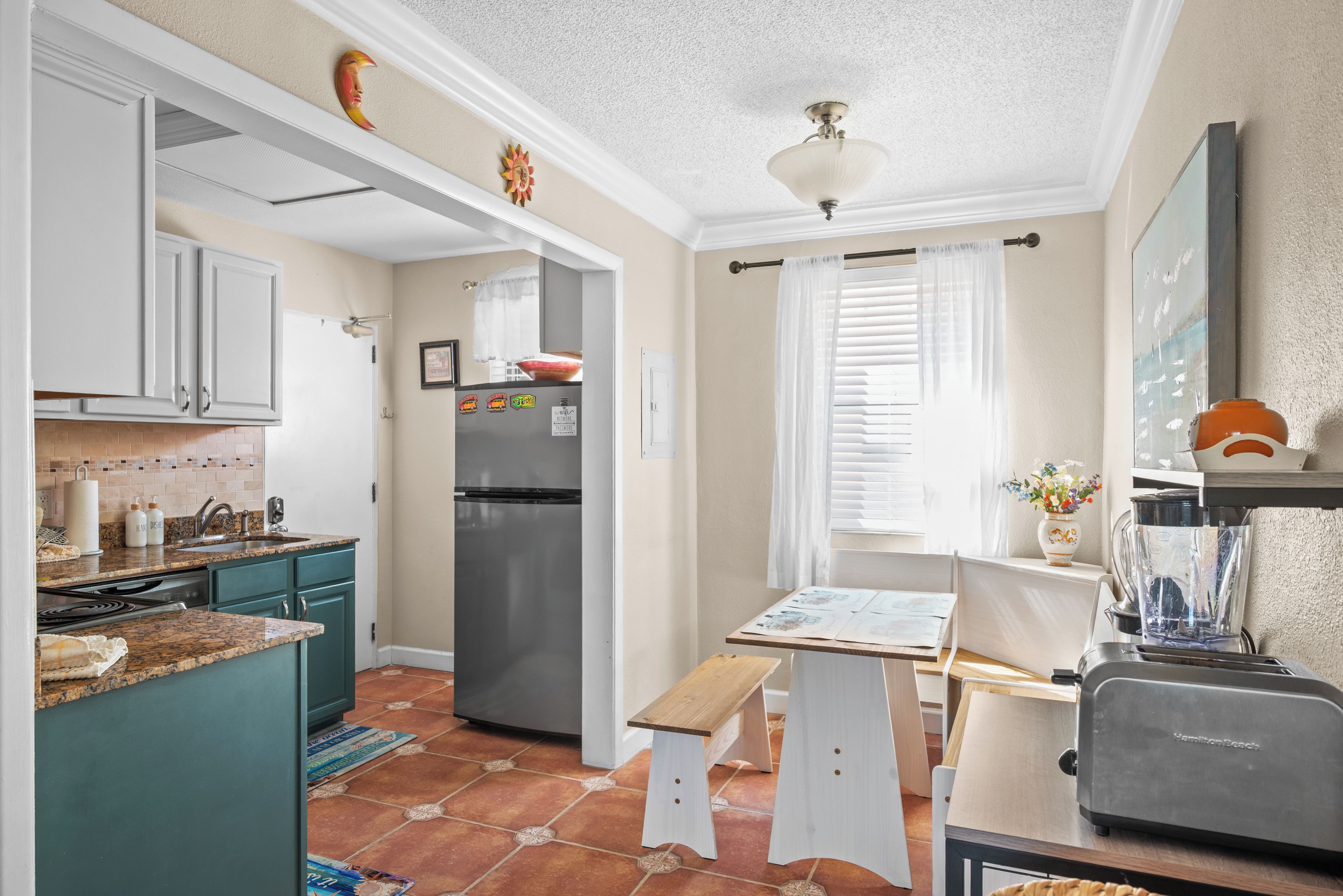 A kitchen with a refrigerator, a sink, and a window with curtains.