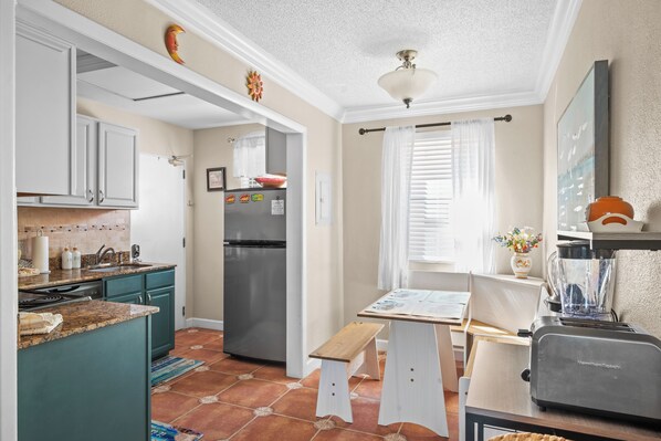 A kitchen with a refrigerator, a sink, and a window with curtains.