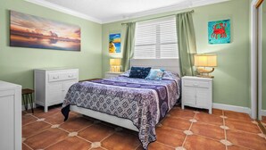 Quarto com cama, mesas de cabeceira, janela com cortinas e obras de arte nas paredes.
