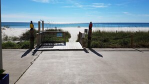 A beach entrance with a wooden gate, a concrete pathway, and a view of the ocean.