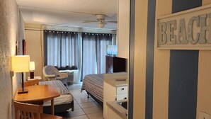 A hotel room with a bed, a desk, a chair, a television, and a sign that says "BEACH".