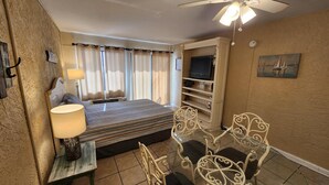 A hotel room with a bed, a TV on a shelf, a dining table with chairs, a ceiling fan, and curtains. - Ambassador 126 - Gulf Front (Panama City Beach)