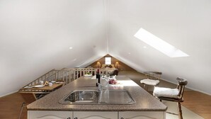 A modern kitchen with a central island, a dining area, and a loft bedroom with a skylight. - Old Mansfield Loft - gardens, gazebo and getaway (Bowral)