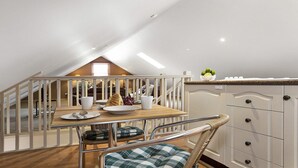 A dining area with a wooden table, white chairs, and a view of a loft bedroom. - Old Mansfield Loft - gardens, gazebo and getaway (Bowral)