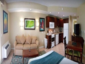 A compact hotel room with a kitchenette, a sofa, a bed, and a dining area.