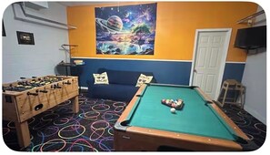 A room with a pool table, foosball table, and colorful circular floor patterns.