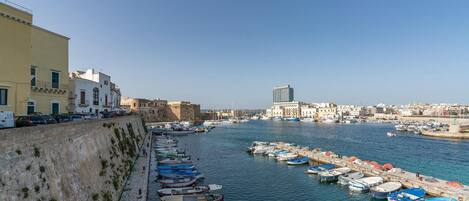 A harbor with boats docked along the quay, a stone wall on one side, and buildings in the background.