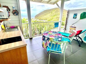 A balcony with a sink, a table with a floral tablecloth, and chairs.