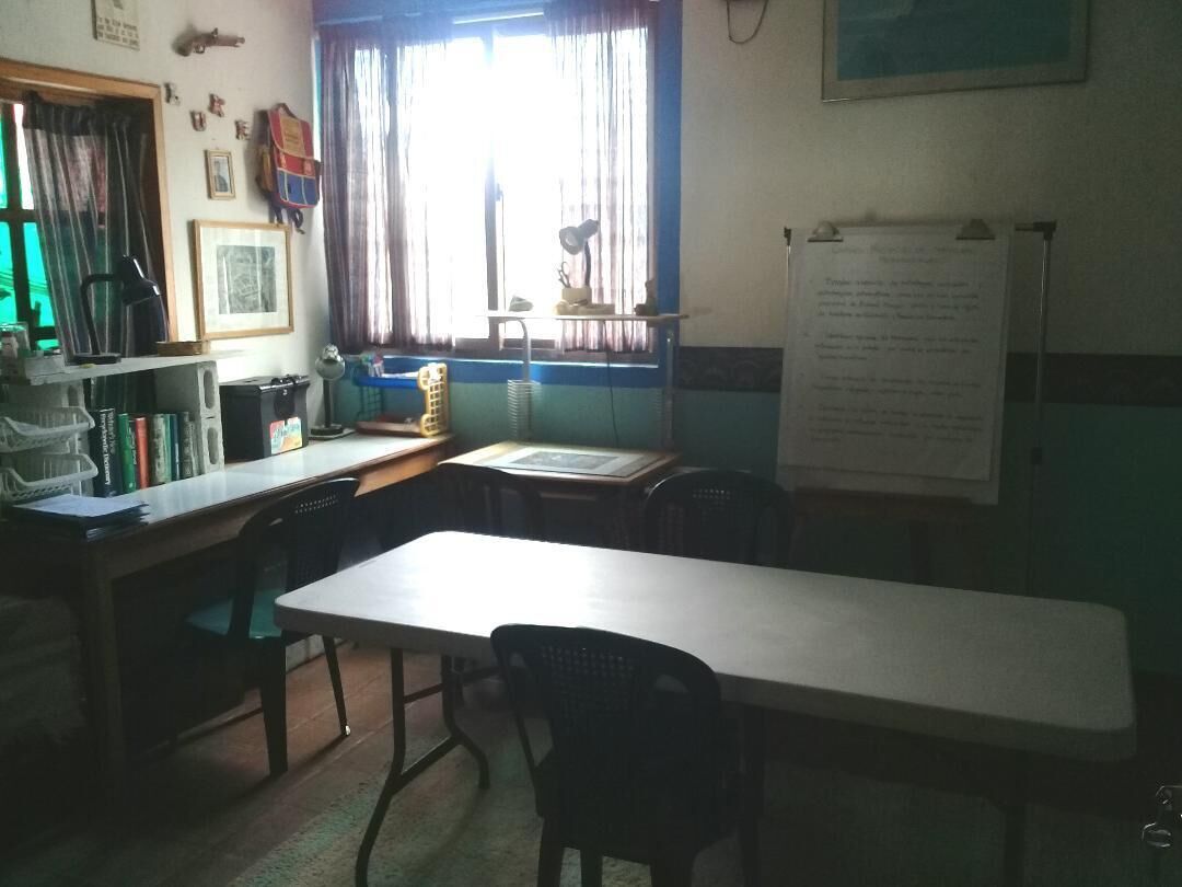 Un aula con una mesa larga, sillas, una pizarra y un ventanal con cortinas.