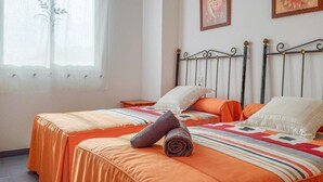 Ein Schlafzimmer mit zwei Betten, einem Fenster mit durchsichtigen Vorhängen und zwei an der Wand befestigten Bildern.