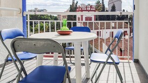 Ein Balkon mit einem weißen Tisch, blauen Stühlen, einer grünen Flasche und einer roten Schüssel.
