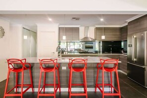 A modern kitchen with a central island, bar stools, stainless steel appliances, and a large window. - Fairways: Spacious Pool House by the Golf Course (Dunsborough)