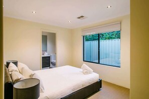 A bedroom with a bed, a nightstand, a lamp, a window with a view, and a door leading to a bathroom.