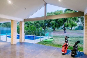 A covered outdoor area with a pool, a golf bag, and a chair. - Fairways: Spacious Pool House by the Golf Course (Dunsborough)