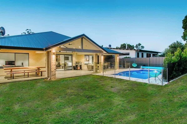 A modern house with a covered patio, a swimming pool, and a barbecue area.