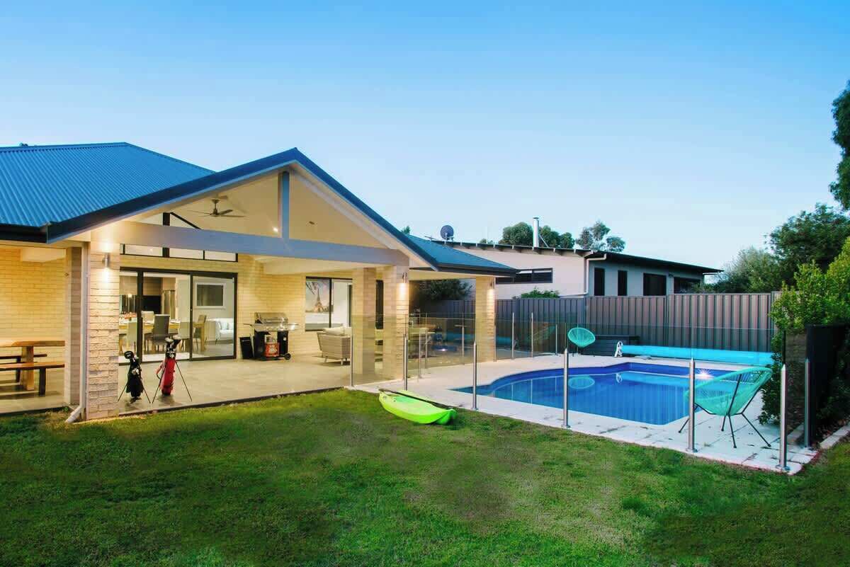 A residential property with a swimming pool, a covered patio, and a grassy backyard.