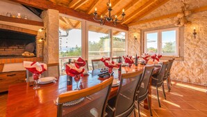 A dining area with a long wooden table set for six, surrounded by chairs with mesh backs. A stone wall and a stone fireplace are visible in the background. - Awesome home in Turanj (Turanj)