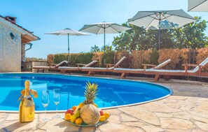 Une piscine avec des chaises longues et des parasols, une bouteille de champagne et une assiette de fruits.