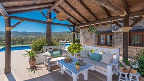 A covered outdoor seating area with a pool, stone walls, and a view of the landscape. - Cortijo Rueda Campos Tolox by Ruralidays (Málaga)