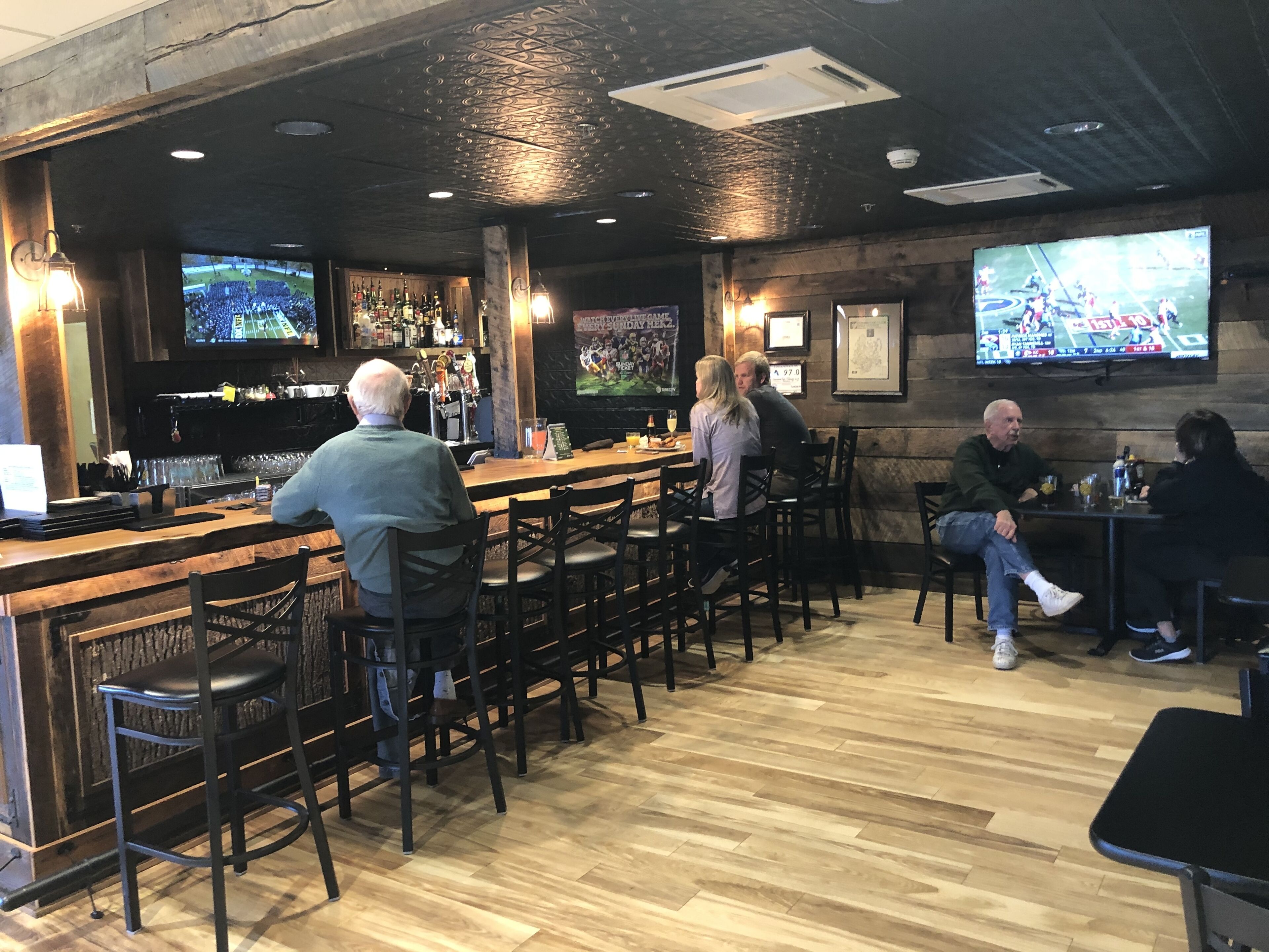 A bar with wooden flooring and a high ceiling with exposed beams. There are multiple screens displaying sports events.