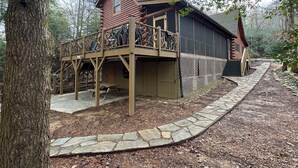 Une cabane en rondins dotée d’une terrasse et d’un chemin de pierre menant à l’entrée.