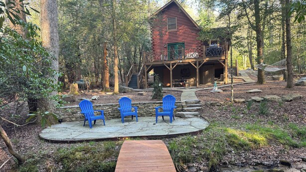 Un chalet rustique doté d’une terrasse en pierre, de deux fauteuils Adirondack et d’un sentier en bois menant à l’entrée.
