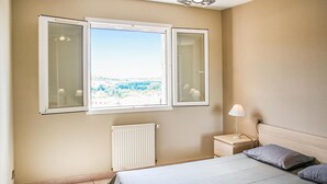 Une chambre à coucher avec un lit, une table de chevet, une lampe, un radiateur et une fenêtre dont les volets sont ouverts.