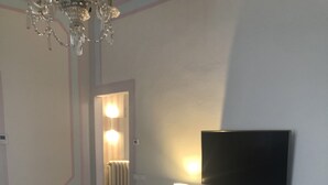 A living room with a sofa, a coffee table, a TV mounted on the wall, a lamp, and a chandelier. - Apartment a stone's throw from the walls (Lucca)