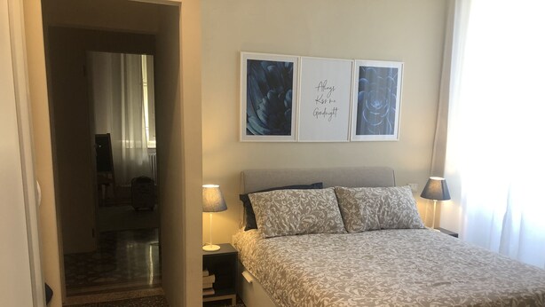 A bedroom with a bed, two bedside tables with lamps, a door leading to another room, and two framed pictures on the wall. - Apartment a stone's throw from the walls (Lucca)